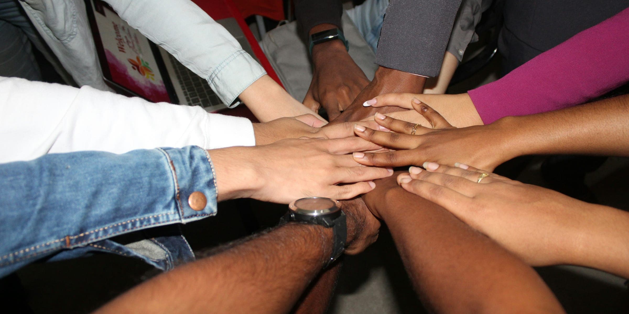 A group of people from different backgrounds stacking their hands together.